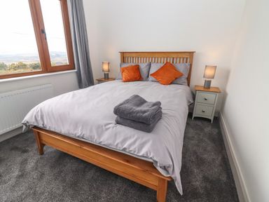 A bedroom with a wooden bed frame gray bedding orange pillows two bedside tables with lamps and a window at Gortnamona in Coolnaharragill Lower near Glenbeigh County Kerry