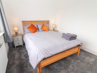 A bedroom with a wooden bed frame gray bedding orange pillows two bedside tables with lamps and folded towels on the bed at Gortnamona in Coolnaharragill Lower near Glenbeigh County Kerry