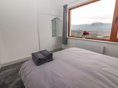 A bedroom with a bed covered with gray bedding a stack of towels on it built in white wardrobes and a large window with a view of hills at Gortnamona in Coolnaharragill Lower near Glenbeigh County Kerry