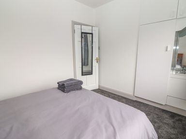 A bedroom with a bed covered in gray sheets and towels on top a white door with a hanging mirror and white built-in wardrobes with a mirror at Gortnamona in Coolnaharragill Lower near Glenbeigh County Kerry