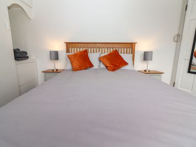 A bedroom with a bed with grey bedding and orange pillows two bedside tables with lamps and a stack of towels at Gortnamona in Coolnaharragill Lower near Glenbeigh County Kerry