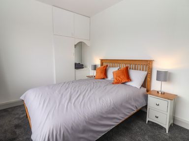 A bedroom with a wooden bed frame orange pillows bedside tables lamps and built in white wardrobes at Gortnamona in Coolnaharragill Lower near Glenbeigh County Kerry