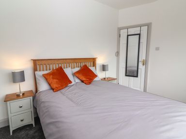 A bedroom with a bed with orange pillows two bedside tables with lamps and a door with a mirror at Gortnamona in Coolnaharragill Lower near Glenbeigh County Kerry