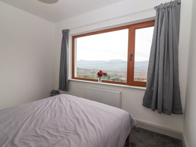 A bedroom with a bed near a window with gray curtains and a vase of flowers at Gortnamona in Coolnaharragill Lower near Glenbeigh County Kerry
