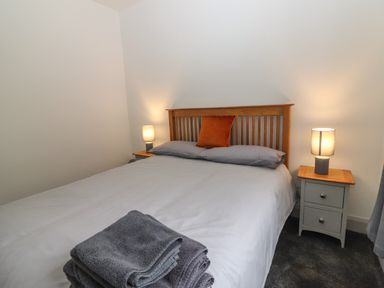 A bedroom with a double bed with grey bedding and an orange pillow with bedside tables and lamps at Gortnamona in Coolnaharragill Lower near Glenbeigh County Kerry