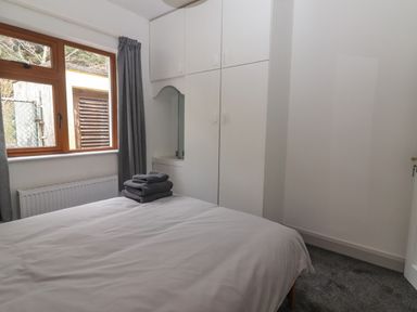 A bedroom with a bed white bedding gray towels on the bed white built in wardrobe and a window with gray curtains at Gortnamona in Coolnaharragill Lower near Glenbeigh County Kerry
