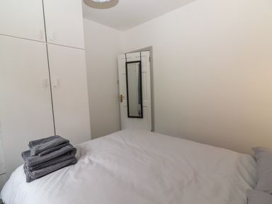 A bedroom with a bed covered in white and gray linens a stack of gray towels on the bed white built-in wardrobes and a door with a hanging mirror at Gortnamona Coolnaharragill Lower near Glenbeigh County Kerry