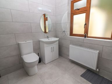 A bathroom with a toilet a sink with cabinet a mirror a radiator and a window at Gortnamona in Coolnaharragill Lower near Glenbeigh County Kerry