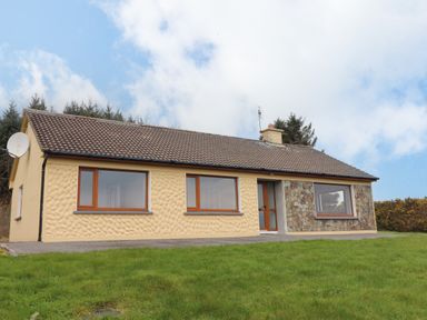 A single-story house with textured yellow walls stone accent and brown tiled roof in a grassy area at Gortnamona in Coolnaharragill Lower near Glenbeigh County Kerry