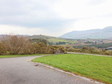 A curved paved road beside a grassy area with bushes and hills in the background at Gortnamona in Coolnaharragill Lower near Glenbeigh County Kerry