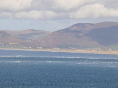 A coastal scene with blue ocean water in the foreground and mountains with scattered houses in the background at Gortnamona Coolnaharragill Lower near Glenbeigh County Kerry