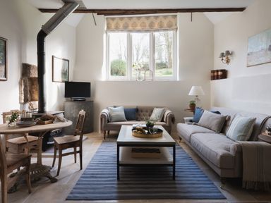 A living room with two sofas a coffee table a blue striped rug a small dining table with wooden chairs and a fireplace at Butterwell Cottage at Collihole in Chagford