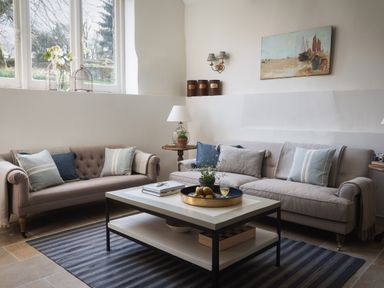 A sitting area with two sofas a coffee table with books and a tray with fruit and a glass a side table with a lamp and a plant and a wall painting at Butterwell Cottage at Collihole in Chagford