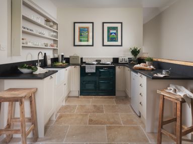 A kitchen with a stove between counters stools and shelves with dishes at Butterwell Cottage at Collihole in Chagford
