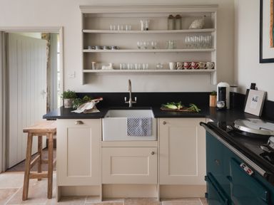 A kitchen with a sink a wooden stool open shelves with cups and glasses and a stove at Butterwell Cottage at Collihole in Chagford