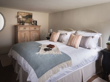 A bedroom with a bed covered with pillows and a blanket a wooden cabinet and two bedside tables with lamps at Butterwell Cottage at Collihole in Chagford