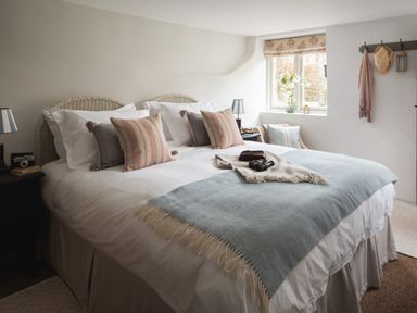 A bedroom with a bed and pillows near a window with a chair and coat hooks at Butterwell Cottage at Collihole in Chagford