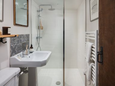 A bathroom with a sink toilet and walk in shower with towels on a heated rail and a wooden door at Butterwell Cottage at Collihole in Chagford