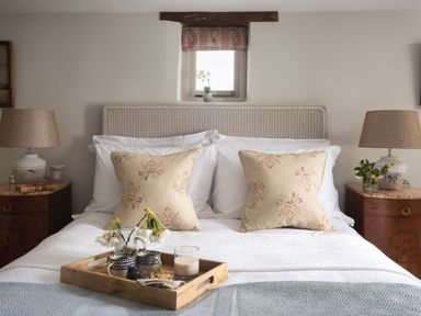A bedroom with a bed with beige pillows a wooden tray with cups and flowers two bedside tables with lamps at Butterwell Cottage at Collihole in Chagford
