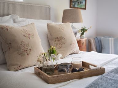 A bed with patterned pillows a wooden tray holding a jug with flowers cups a glass with milk and figs at Butterwell Cottage at Collihole in Chagford