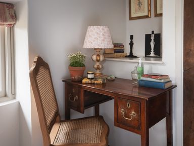 A wooden desk with books lamp plant and hand sanitizer next to a wooden chair with cane seat and back at Butterwell Cottage at Collihole in Chagford