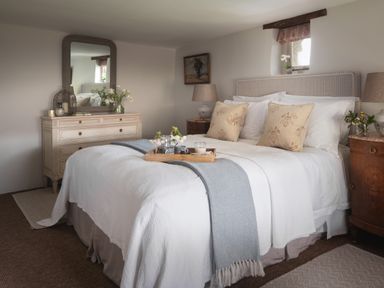 A bedroom with a bed tray floral cushions dresser and lamps at Butterwell Cottage at Collihole in Chagford