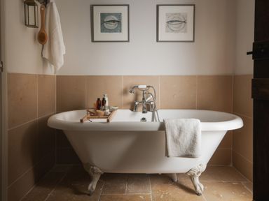 A bathroom with a clawfoot bathtub with bath accessories on a wooden tray and two framed artworks on the wall at Butterwell Cottage at Collihole in Chagford