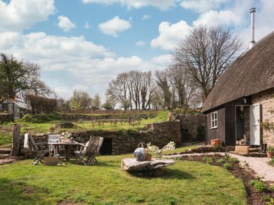 A garden with wooden chairs and table near a stone cottage with thatched roof at Butterwell Cottage at Collihole in Chagford