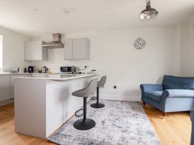 A kitchen with a white island and two stools next to a blue armchair on a rug at Chynoweth House in Cubert