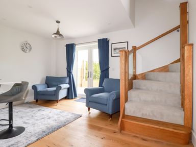 A sitting area with two blue armchairs near glass doors and carpeted stairs with wooden banisters at Chynoweth House in Cubert