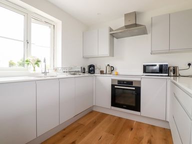 A kitchen with white cabinets a window a sink an oven a microwave a toaster and a kettle at Chynoweth House in Cubert