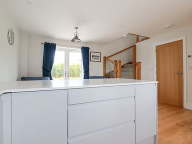 A kitchen island with white drawers in an open room with a staircase wooden door and sliding glass doors with blue curtains at Chynoweth House in Cubert
