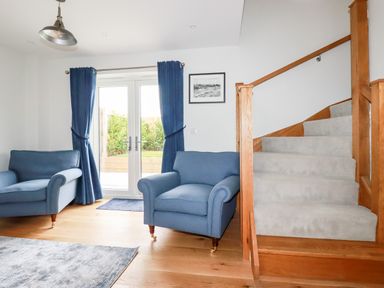 A living room with blue armchairs blue curtains carpeted stairs and a framed picture at Chynoweth House in Cubert