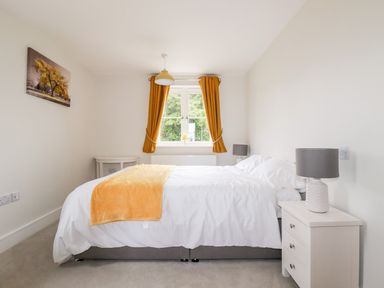 A bedroom with a bed white bedding a yellow throw two bedside tables lamps yellow curtains and a window at Chynoweth House in Cubert
