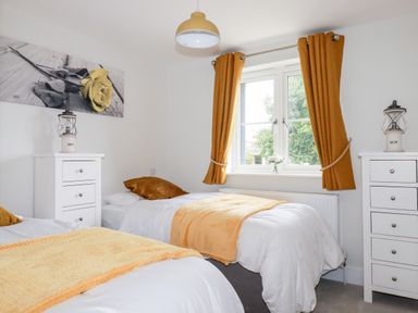 A bedroom with two single beds yellow curtains and dressers at Chynoweth House in Cubert