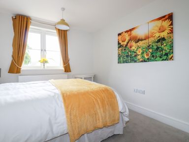 A bedroom with a bed covered in white and yellow bedding a window with mustard curtains and a sunflower painting on the wall at Chynoweth House in Cubert