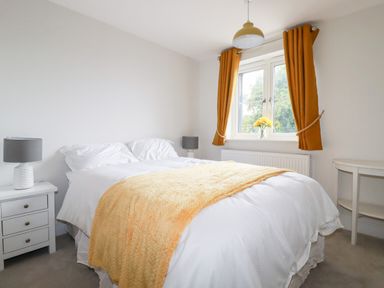 A bedroom with a double bed white bedding a yellow blanket bedside tables with lamps and a window with yellow curtains at Chynoweth House in Cubert