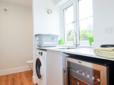 A laundry room with a washing machine laundry basket sink and wine fridge at Chynoweth House in Cubert