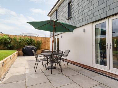 A patio with a round table and four chairs under a green umbrella next to a building with glass doors at Chynoweth House in Cubert