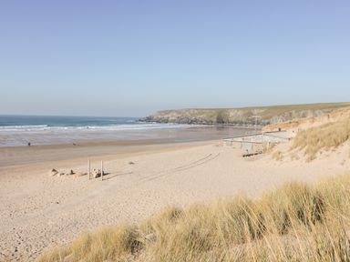 A sandy beach with grass in the foreground a building near the shore and cliffs in the background at Chynoweth House in Cubert