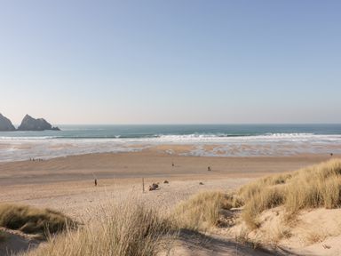 A sandy beach with dunes in the foreground and ocean waves in the background at Chynoweth House in Cubert