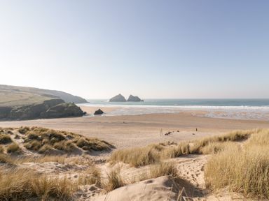 A sandy beach with grass-covered dunes and rock formations in the ocean at Chynoweth House in Cubert