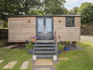 An outdoor wooden cabin with black double doors stone stairs and flower pots at Shepherds Stone in Llanfairynghornwy near Llanfaethlu