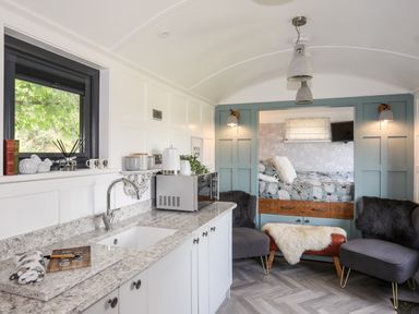 A kitchen area with a countertop, sink, microwave, two chairs, and a bed alcove with blue paneling at Shepherd's Stone in Llanfairynghornwy near Llanfaethlu