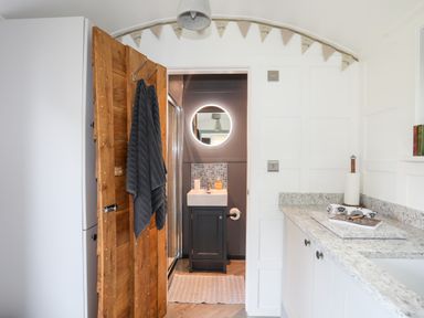 A bathroom with a wooden door and towels hanging on it a sink with a round mirror and patterned tiles at Shepherd's Stone in Llanfairynghornwy near Llanfaethlu