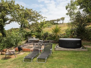 An outdoor garden area with two lounge chairs a circular table with chairs a small grill a fire pit and an inflatable hot tub at Shepherd's Stone in Llanfairynghornwy near Llanfaethlu