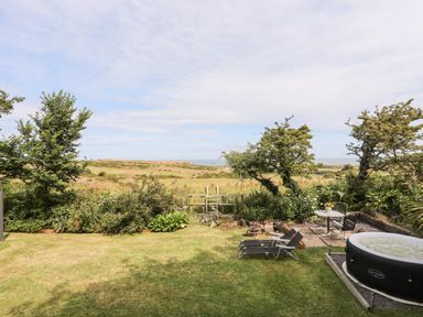 A garden with lounge chairs a small table and inflatable hot tub overlooking fields and trees at Shepherd's Stone in Llanfairynghornwy near Llanfaethlu