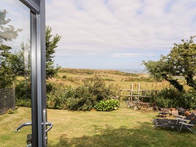 A garden with chairs and a fire pit overlooking fields and hills at Shepherd's Stone in Llanfairynghornwy near Llanfaethlu