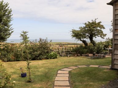 A garden with a stone pathway and lawn chairs overlooking the sea at Shepherd's Stone in Llanfairynghornwy near Llanfaethlu
