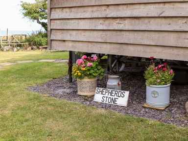 Two flower pots and a milk can with a shepherds stone sign under a wooden structure at Shepherds Stone in Llanfairynghornwy near Llanfaethlu